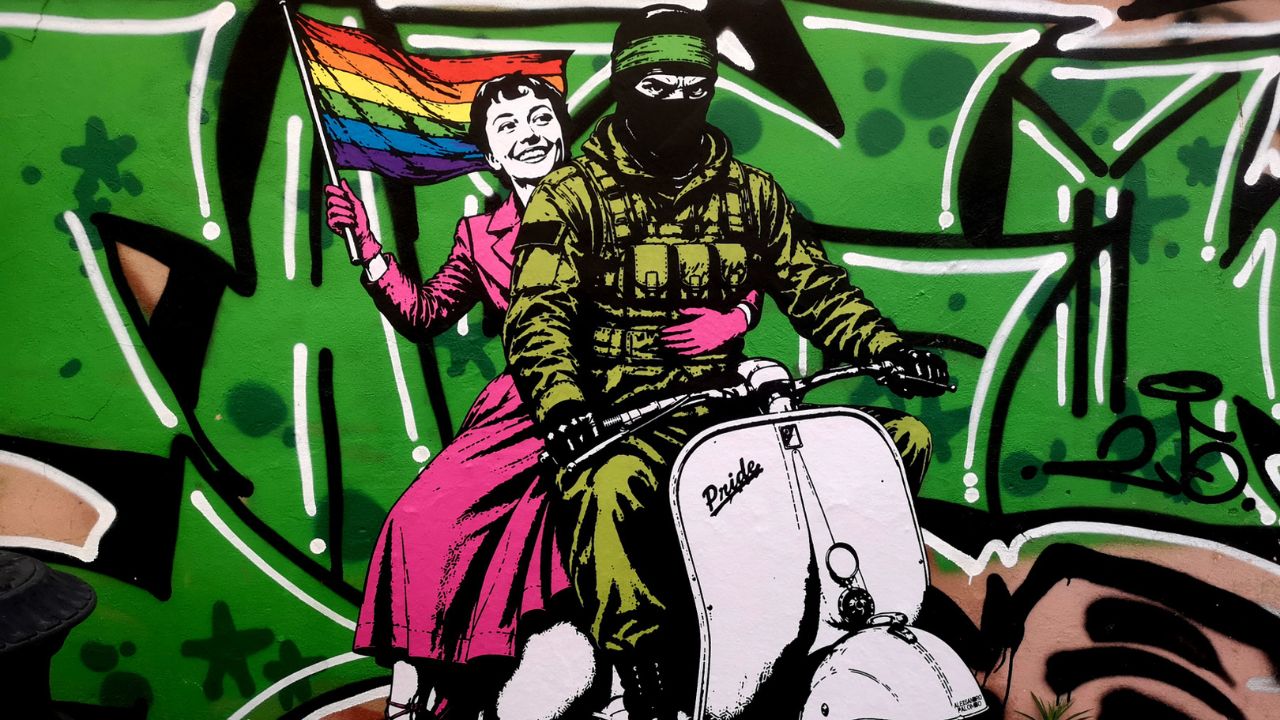 Vandalizzata a Roma l’opera di aleXsandro Palombo con Audrey Hepburn e un miliziano di Hamas: sfregiata la bandiera Pride